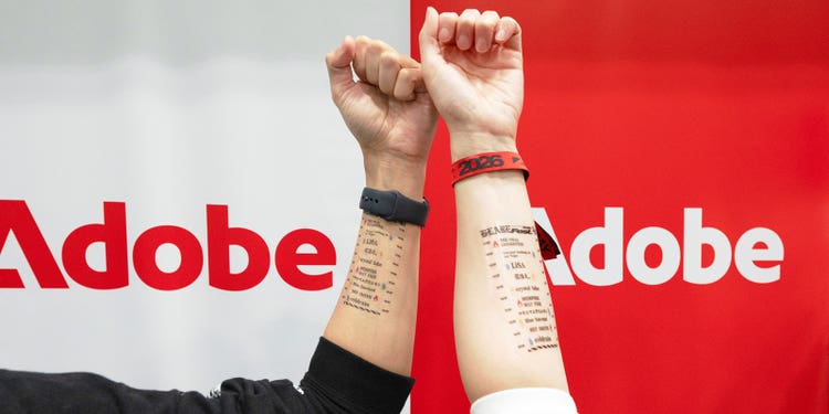 アドビのロゴを背景に掲げられたタトゥーシールを貼った2人の腕